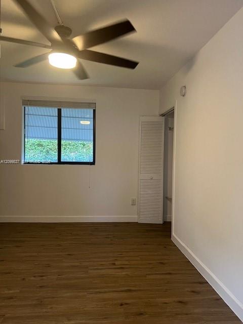 Empty bedroom with wood-look flooring, ceiling fan, window, and louvered closet door.