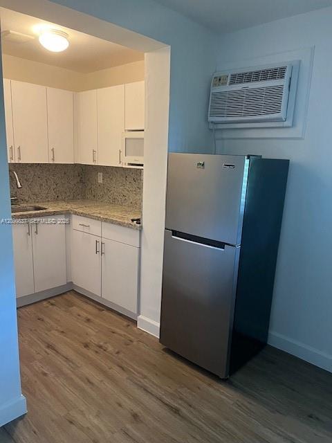 Compact kitchen with white cabinets, speckled stone counters, a stainless steel refrigerator, and wood-look flooring.