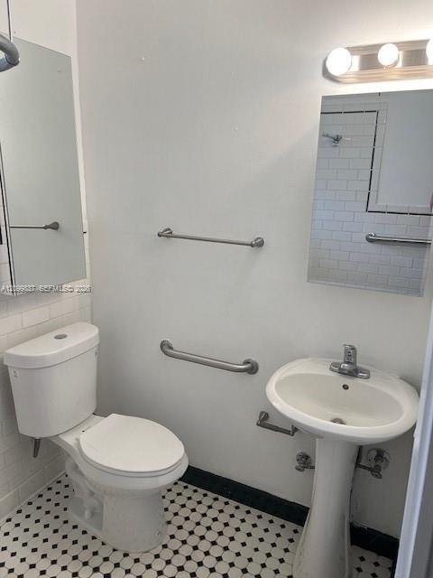 Bathroom with a pedestal sink, grab bars, and black-and-white hexagonal floor tiles.