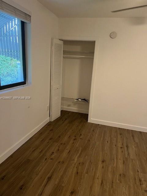 Empty bedroom with wood-look flooring, a window with blinds, and an open closet.