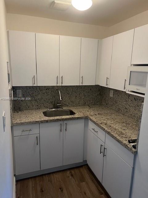 Vacant kitchen with white cabinets, granite counters, a stainless steel sink, and wood-look flooring.