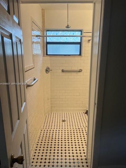 Shower stall with cream tile walls, mosaic floor, window, and metal grab bars.