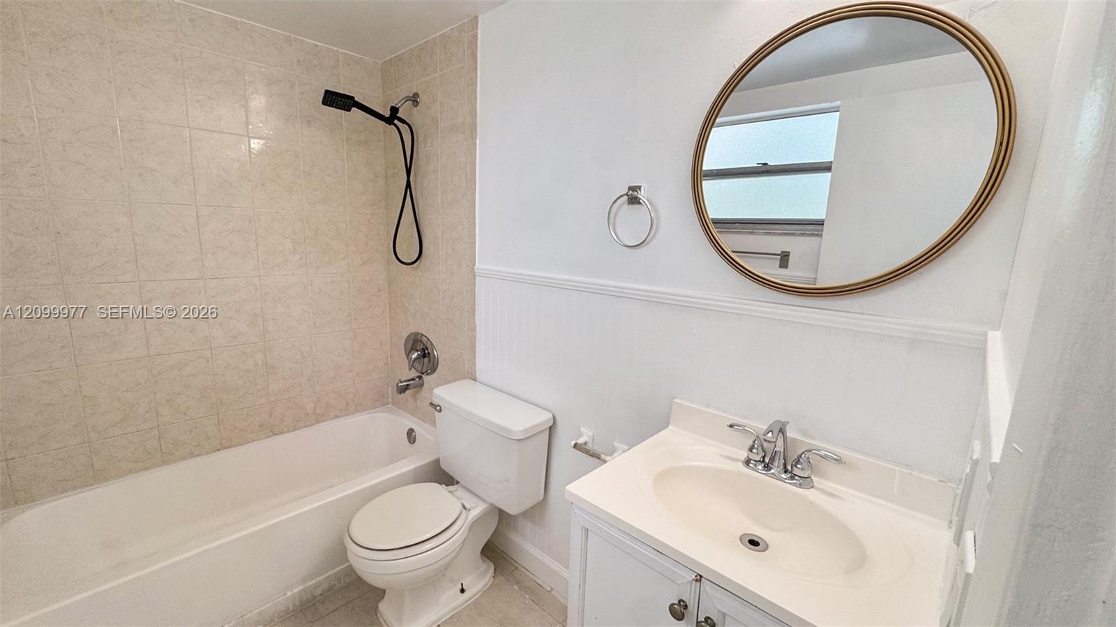 Bathroom with beige tile around the tub, a white vanity, and a large round mirror.