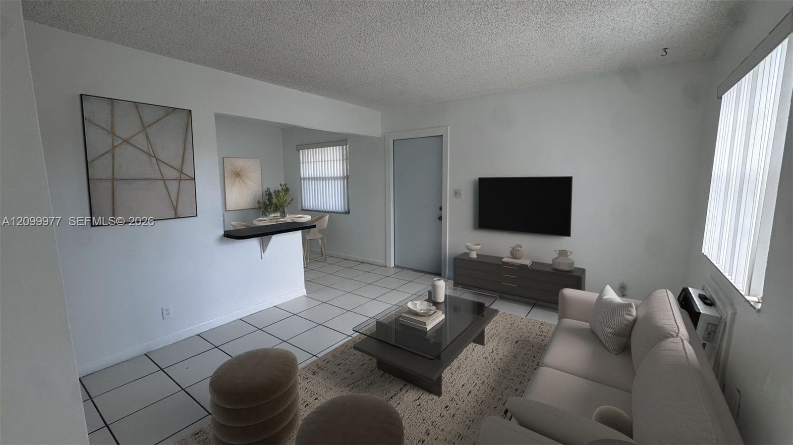 Staged condo living room with a light sofa, glass coffee table, and tiled floor.