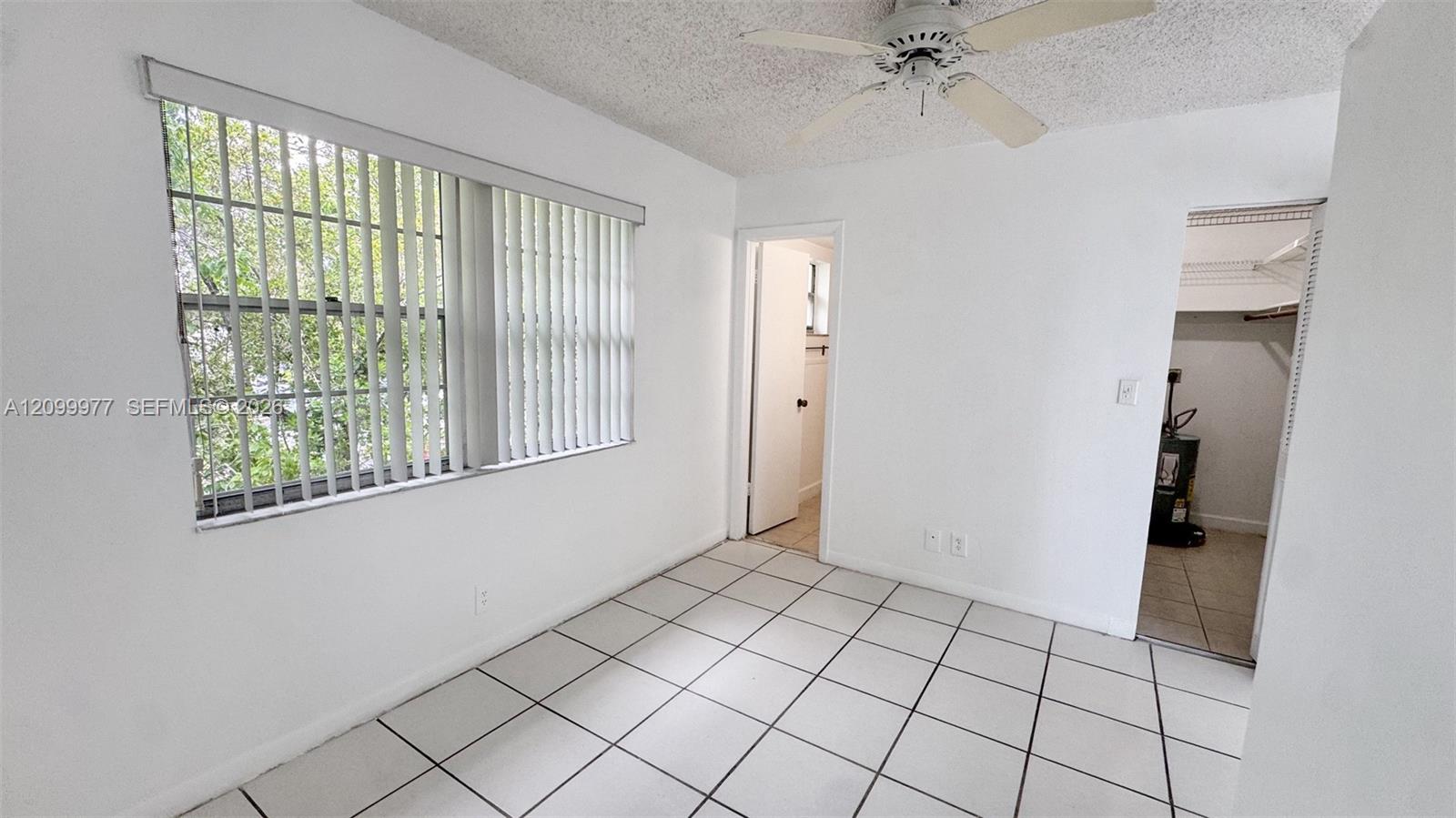Unfurnished bedroom with tiled floor, a large window with vertical blinds, and an open closet.