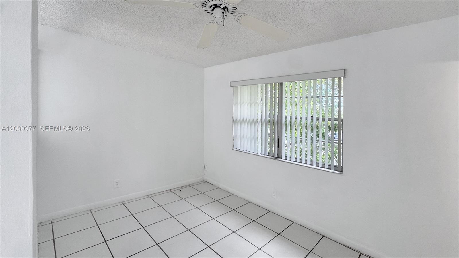 Empty white room with square tile flooring, a ceiling fan, and a window with vertical blinds.