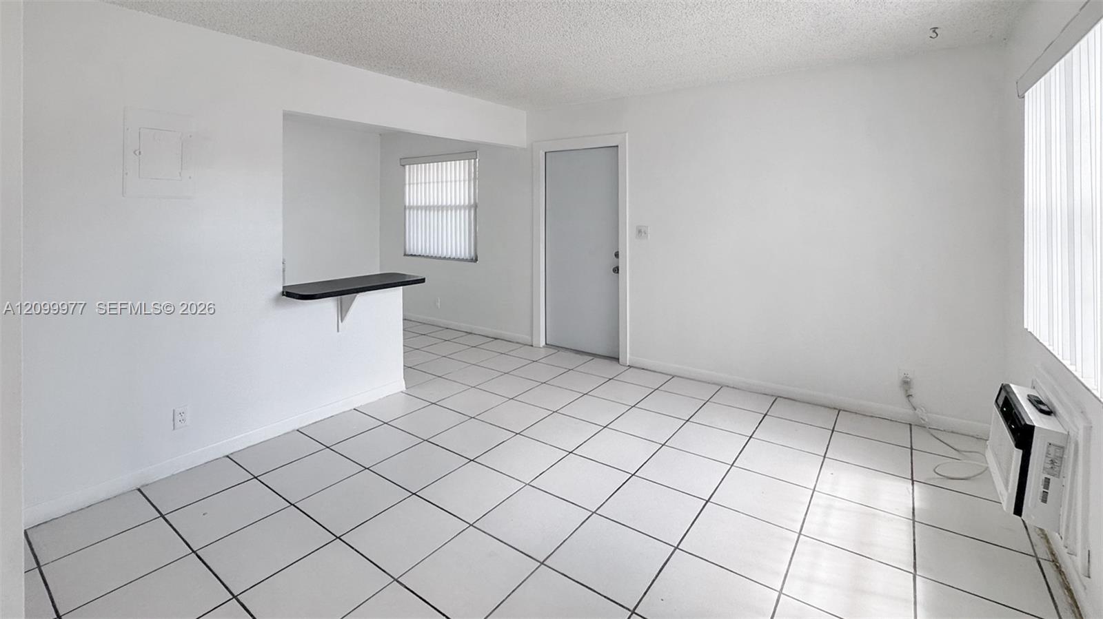 Vacant tiled room with vertical blinds, a black pass-through counter, and a wall-mounted air conditioner.