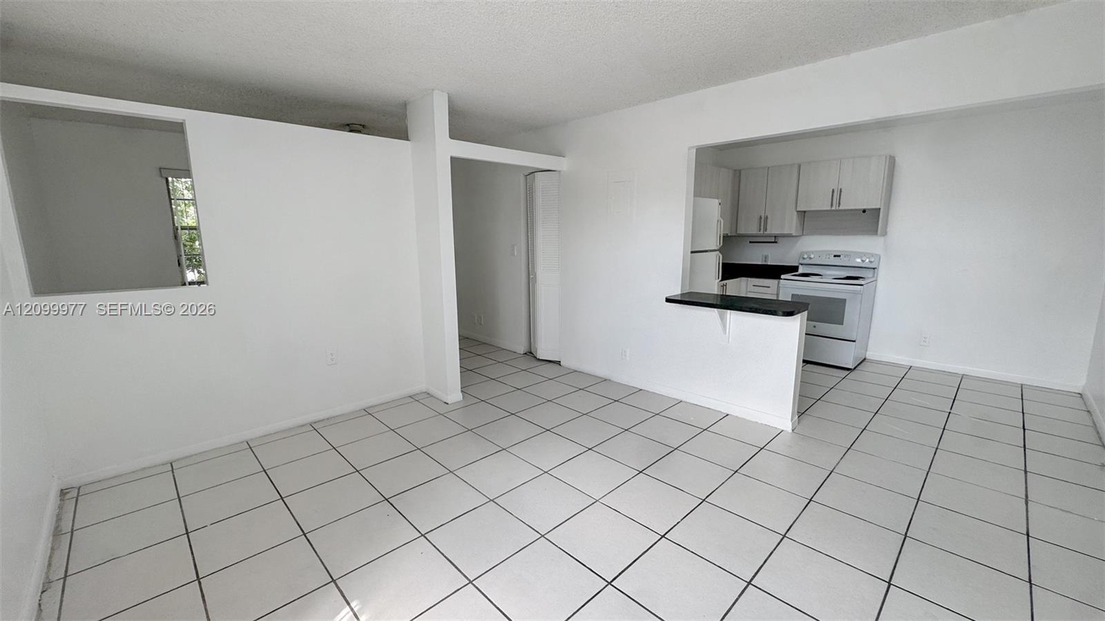 Open condo kitchen with white cabinets, a dark breakfast bar, and tiled floors.