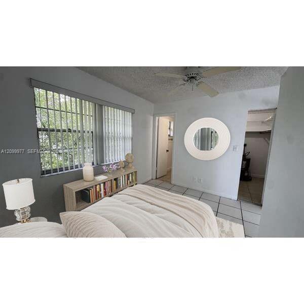 Bedroom with a bed, broad windows with vertical blinds, a bookcase, and a round wall mirror.