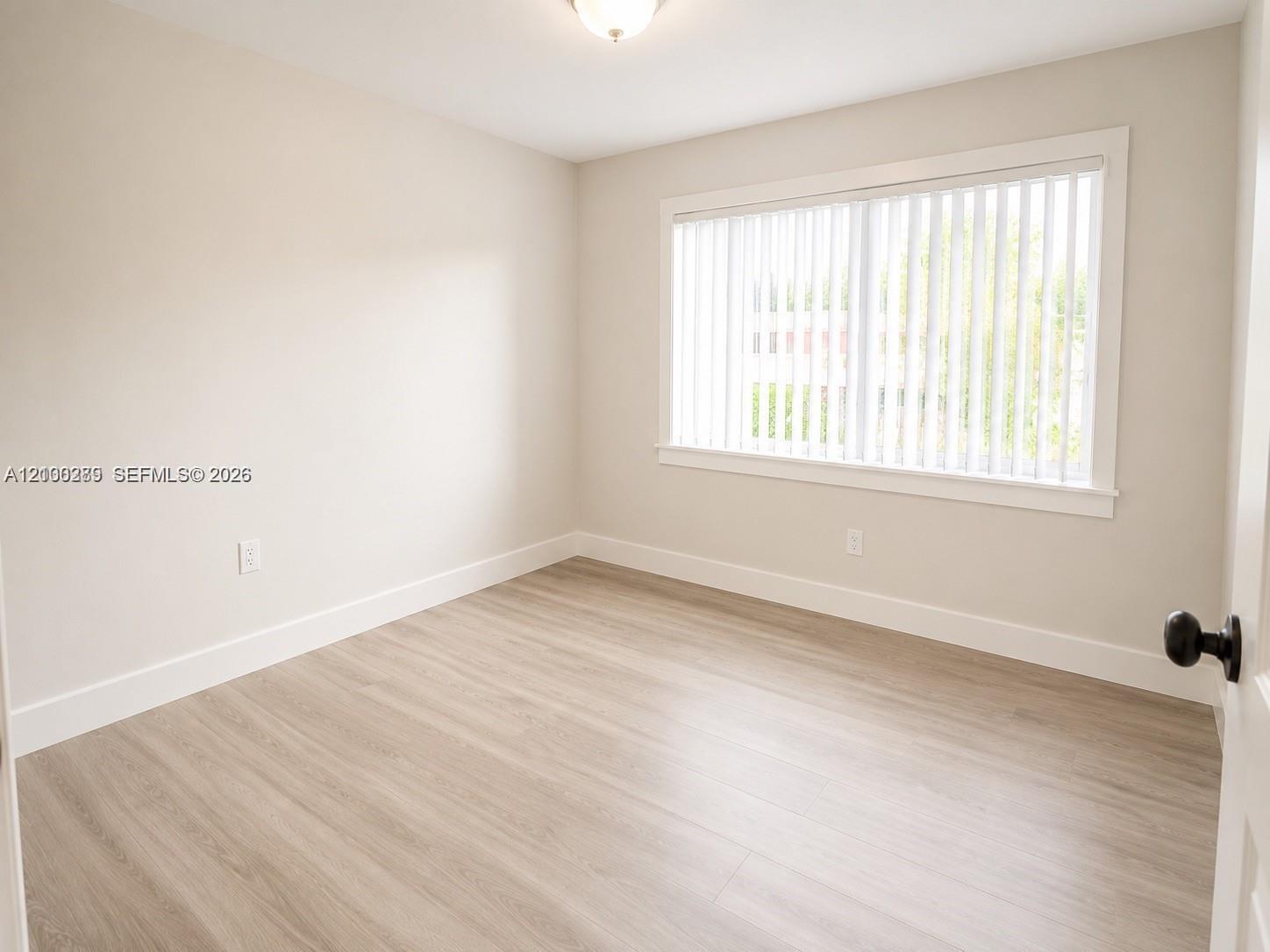Empty room with light wood-look flooring and a large window with vertical blinds.
