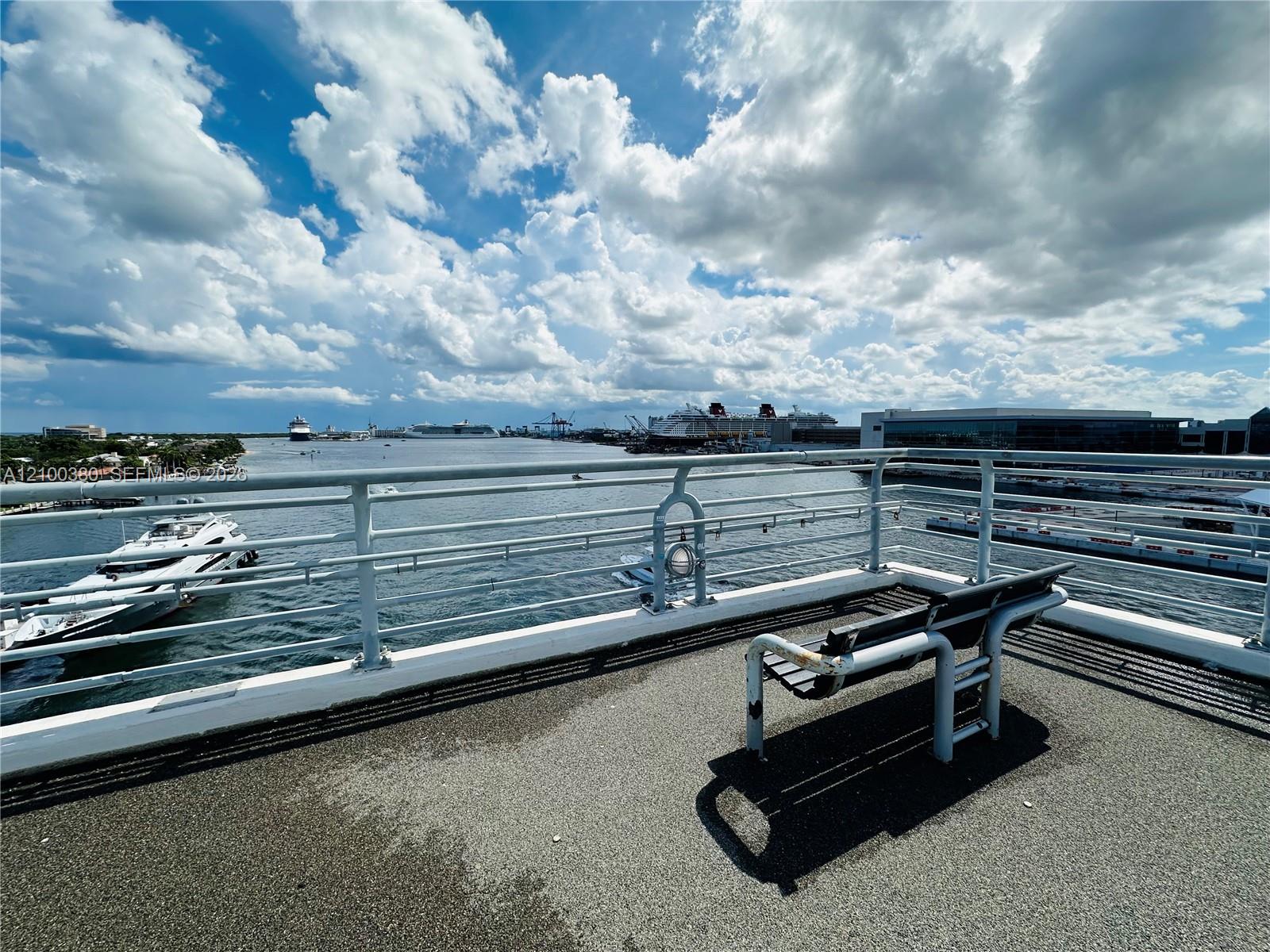 Waterfront view from a paved terrace, with cruise ships across the water and white railings in the foreground.