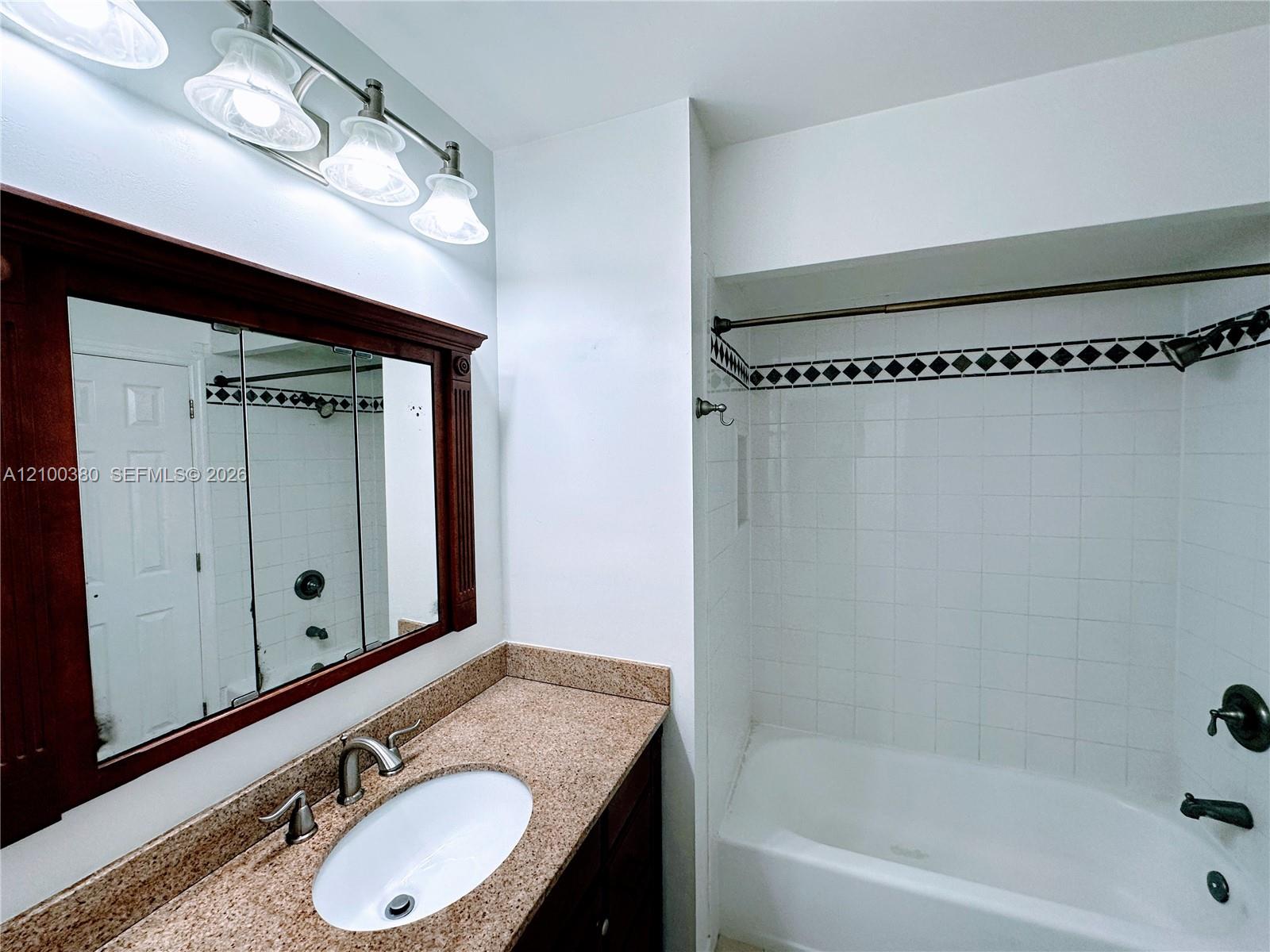 Bathroom with granite vanity, dark wood-framed mirror, and tiled tub and shower.