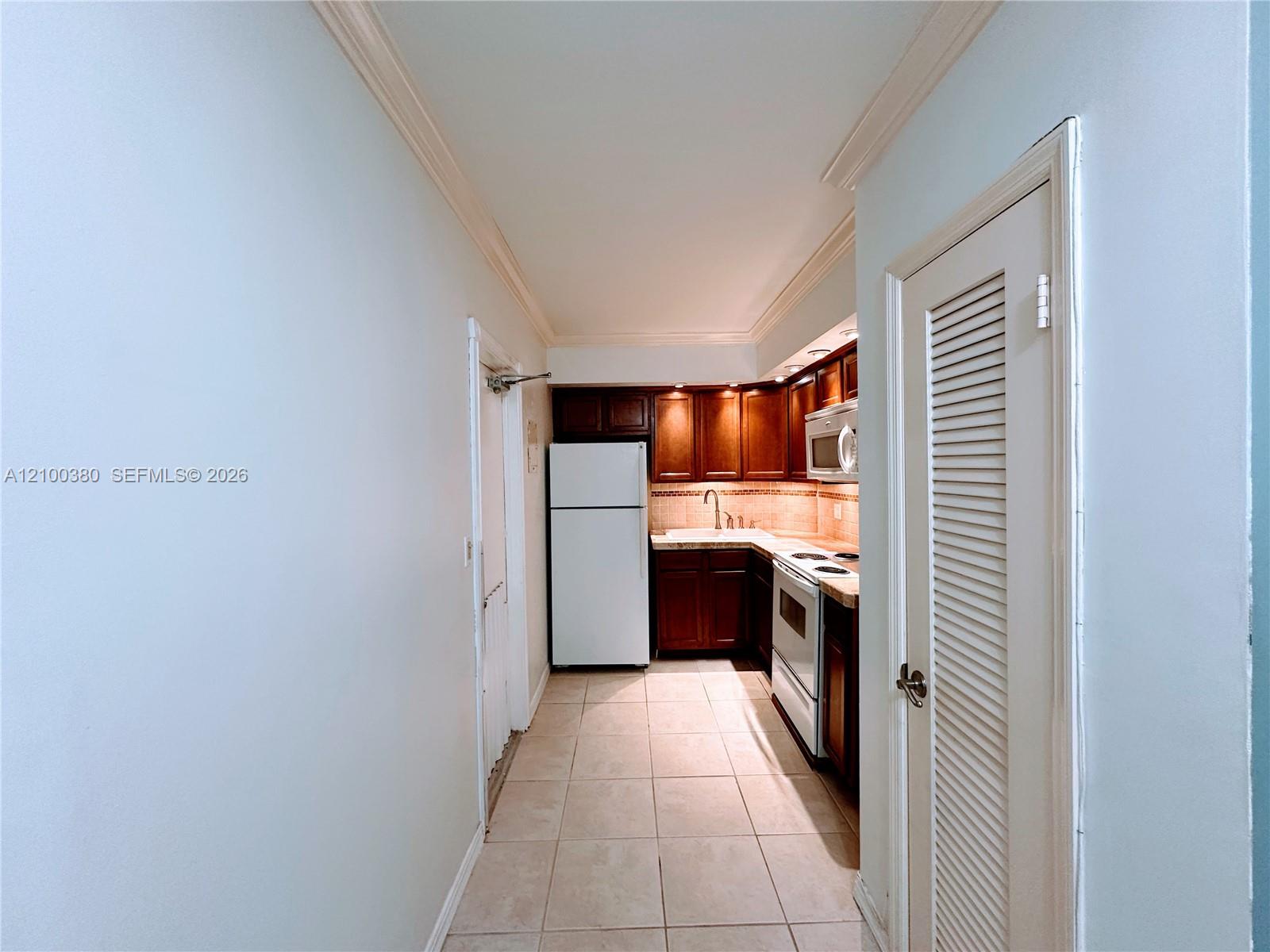Compact kitchen with dark wood cabinets, tiled floors, and white appliances.