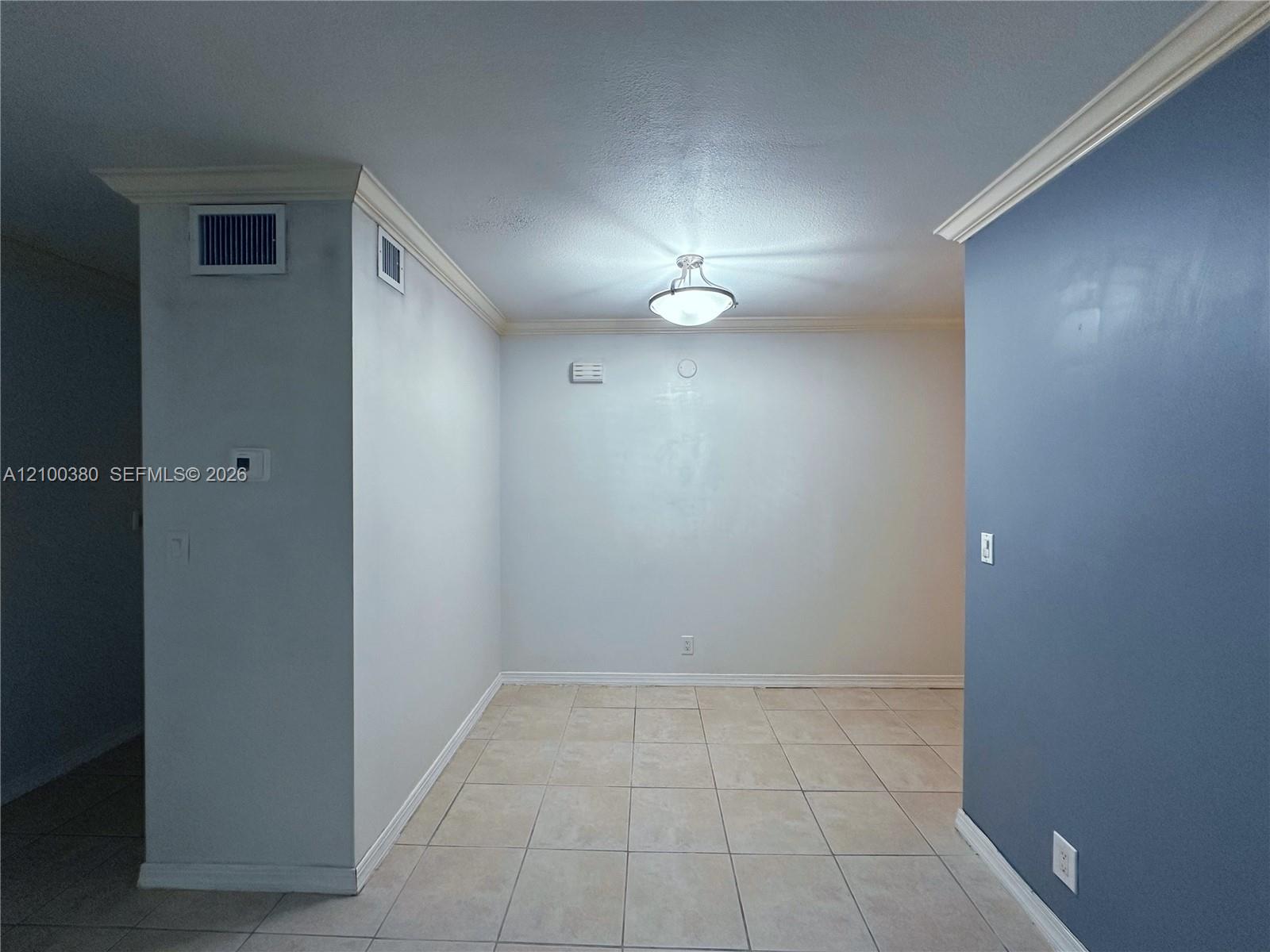Empty tiled room with a blue accent wall, crown molding, and ceiling light.