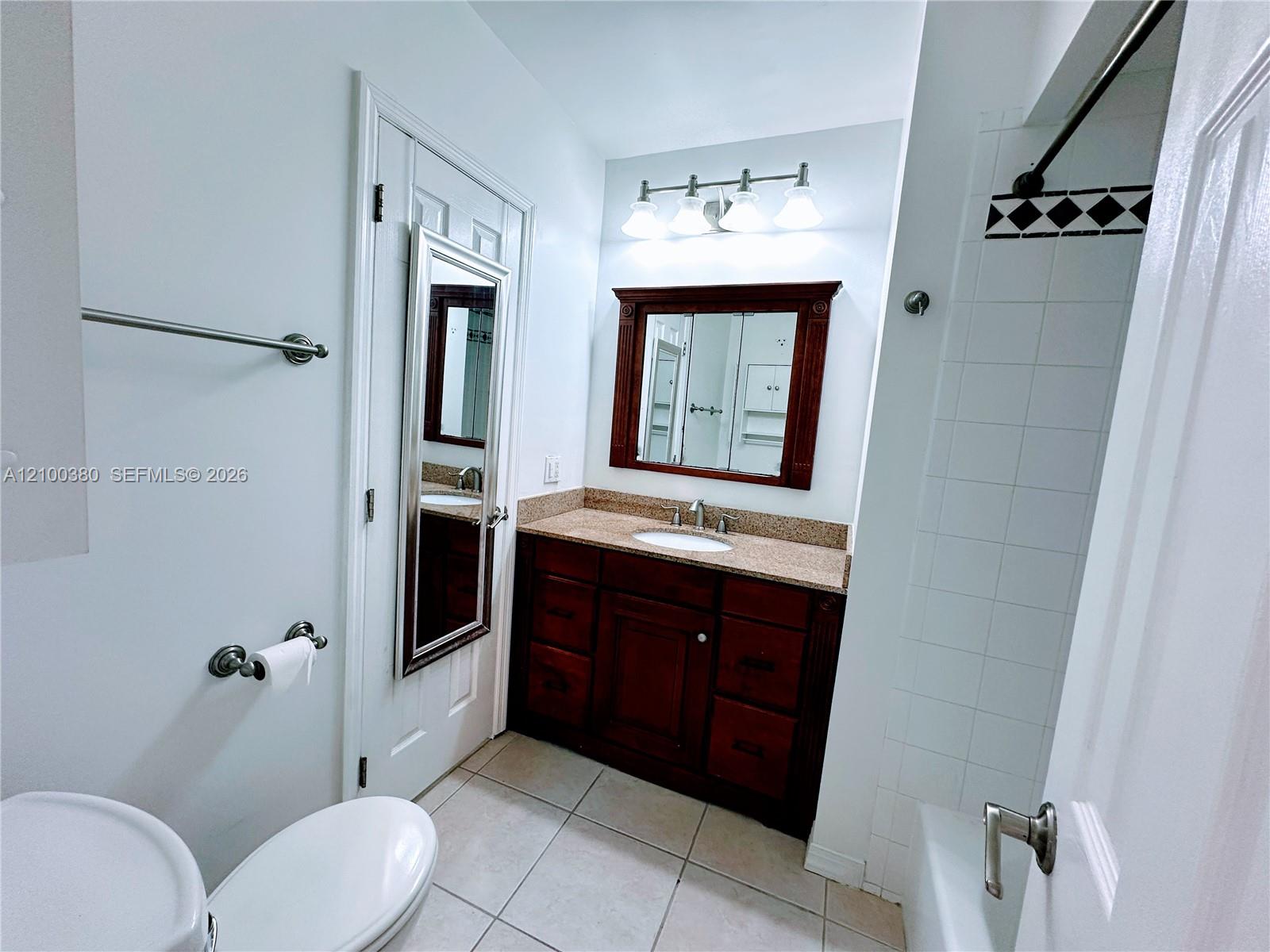 Bathroom with a dark wood vanity, stone countertop, framed mirror, and tiled tub-shower.