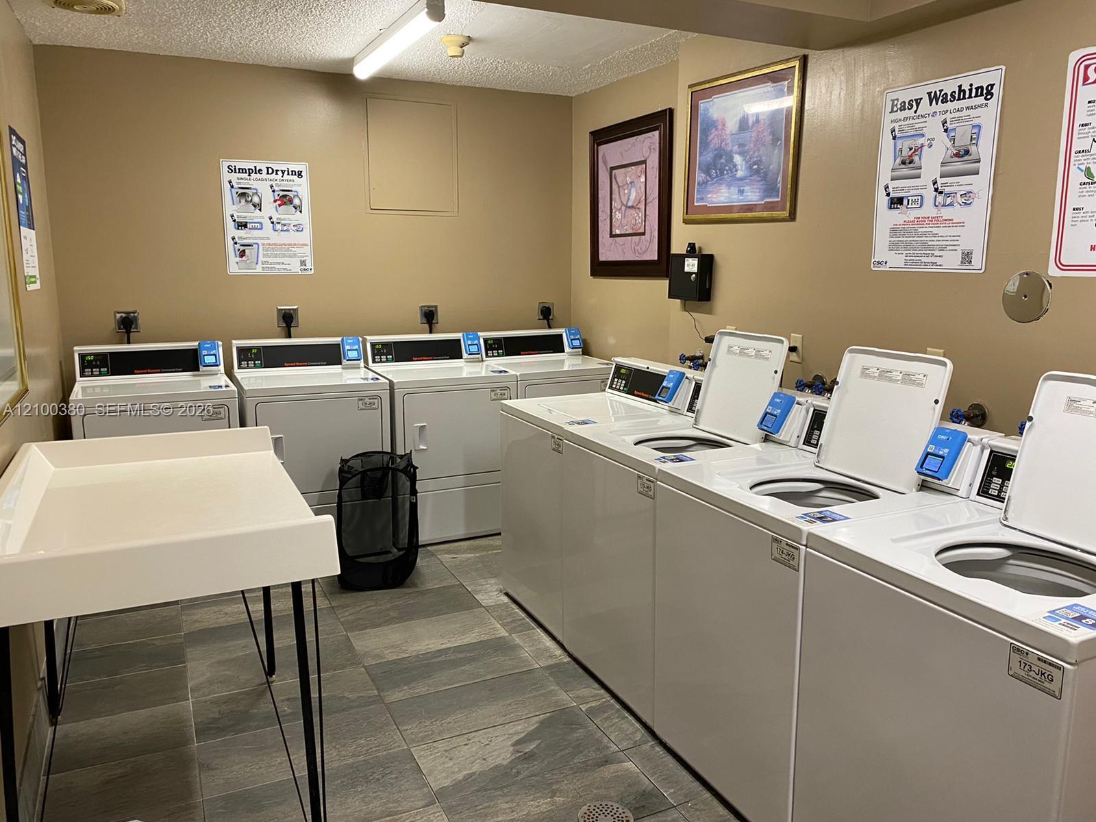 Communal laundry room with rows of white washers and dryers and a utility sink.