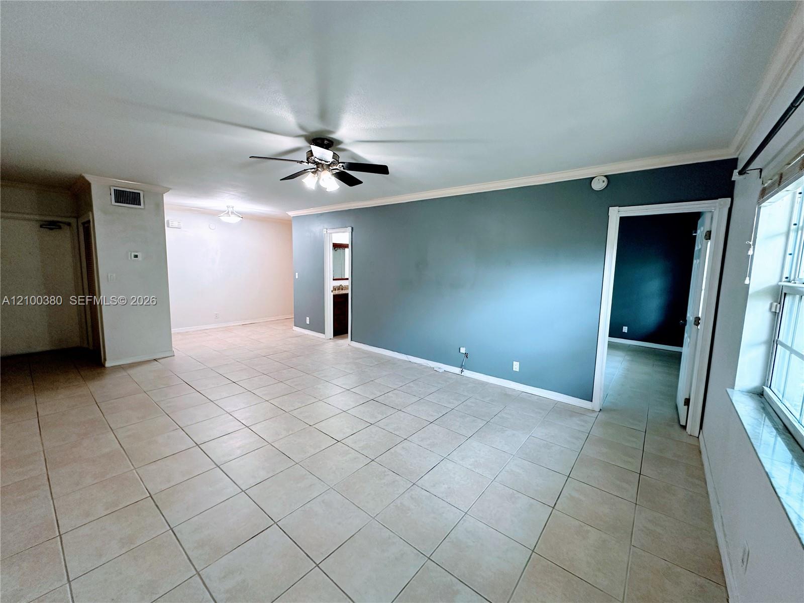 Unfurnished tiled living room with a blue-gray accent wall, ceiling fan, and large windows.