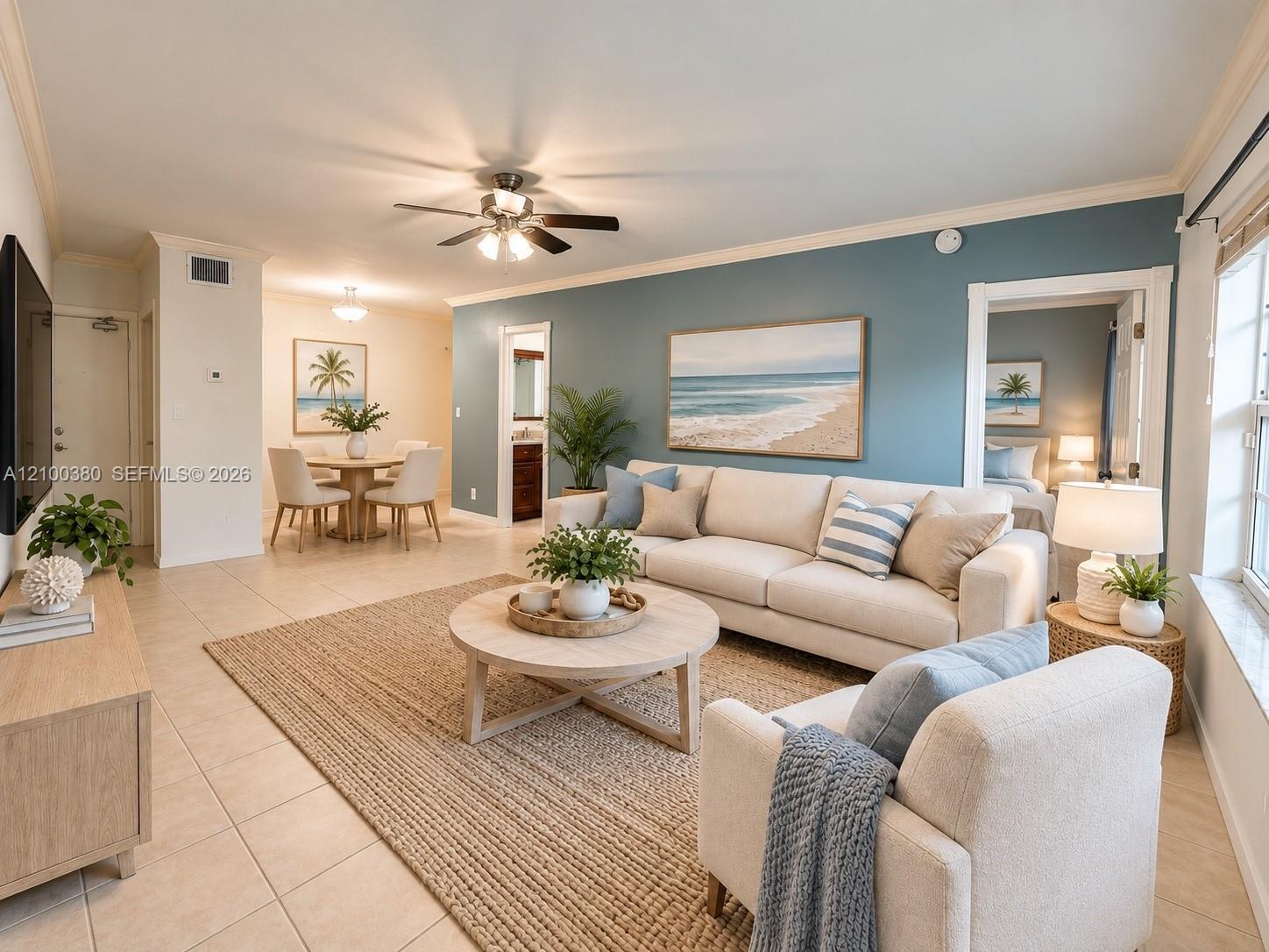 Living room with cream sofas, a blue accent wall, and beach artwork beside a dining area.