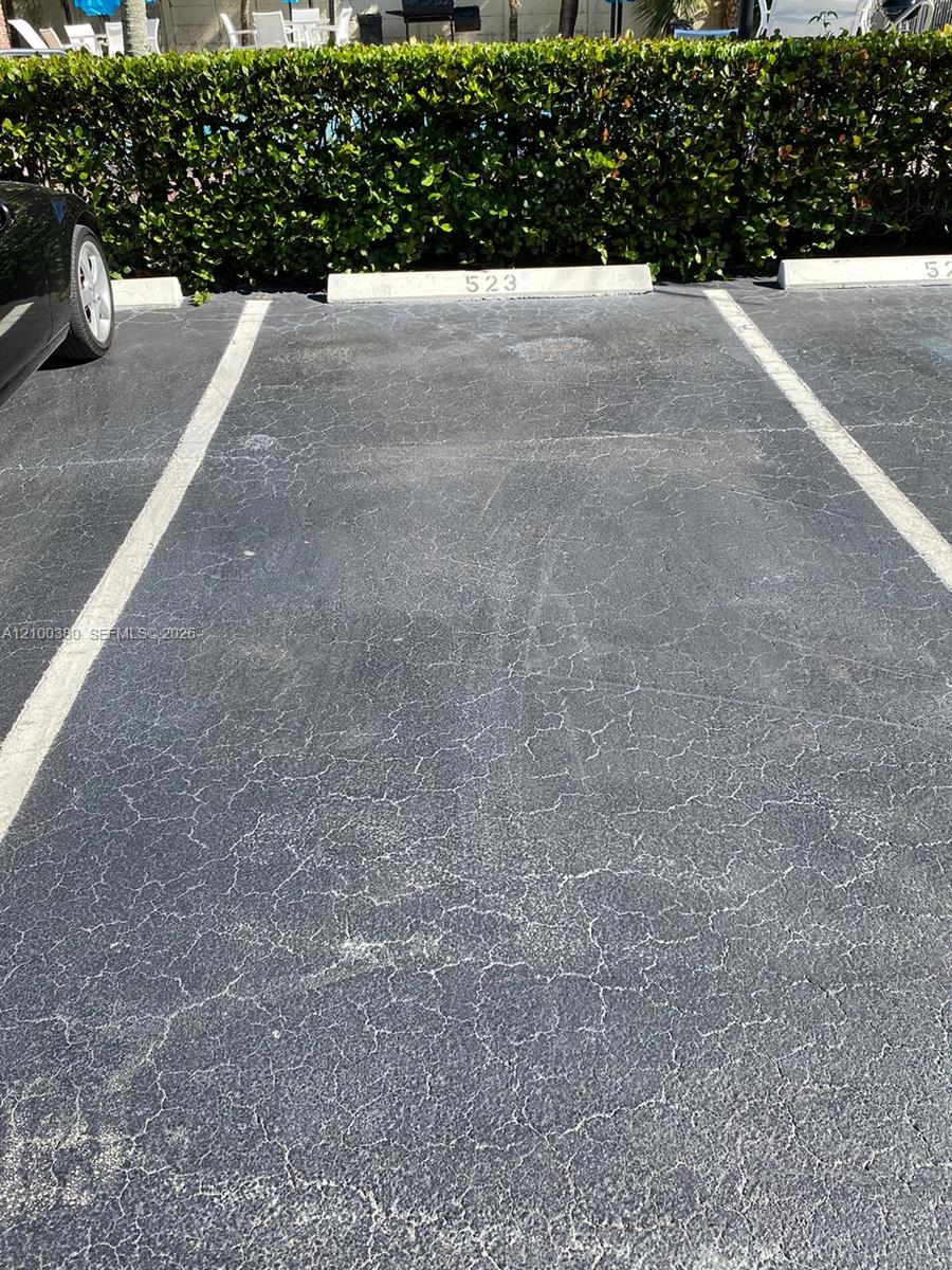 Parking space 523 with cracked asphalt and a tall hedge behind it.