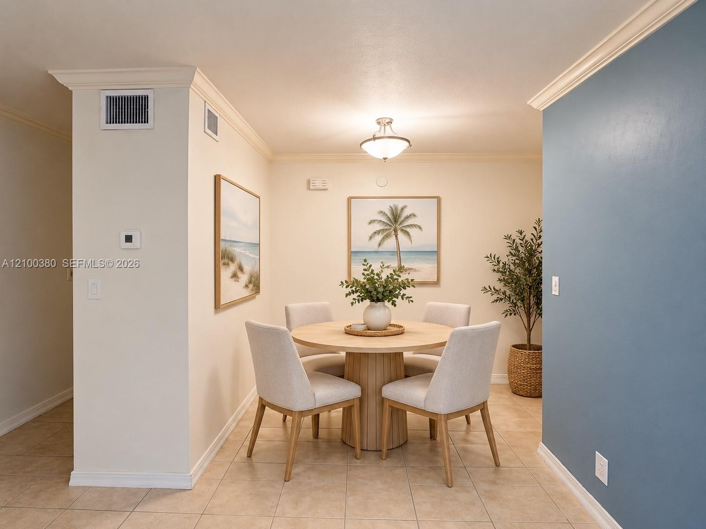 Dining area with a round wood table, four upholstered chairs, tropical artwork, and a blue accent wall.