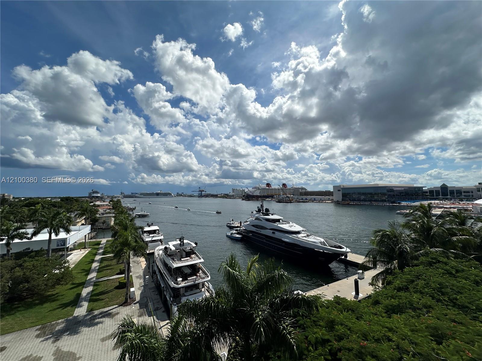 Waterway view with yachts, cruise ships, and palm-lined docks beneath dramatic clouds.