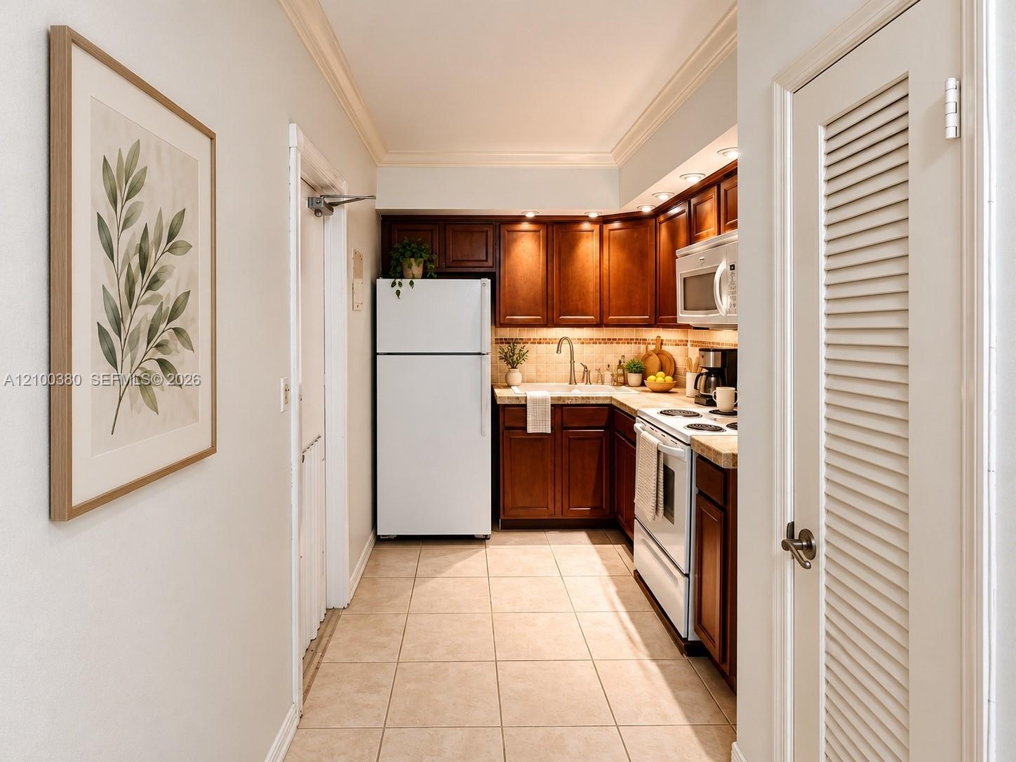 Galley kitchen with dark wood cabinets, white appliances, tile floors, and framed botanical art.