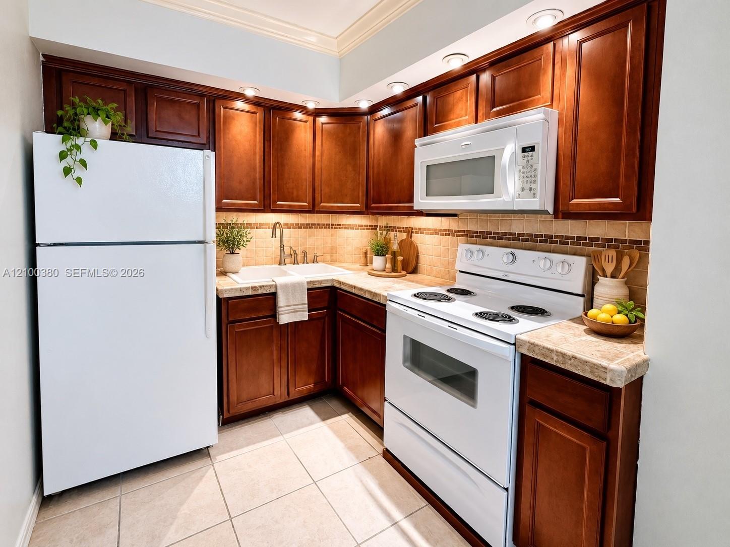 Condo kitchen with dark wood cabinets, white appliances, beige tile counters, and a corner sink.