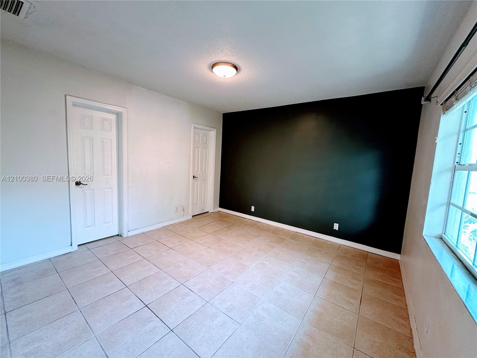 Empty tiled room with a dark accent wall, two doors, and a window.