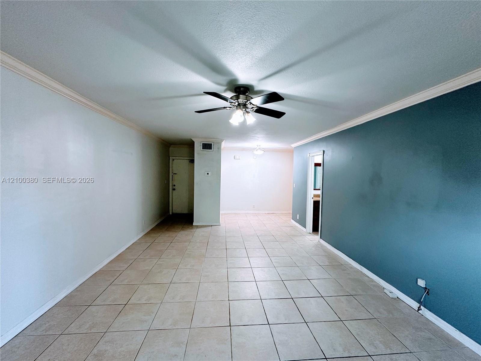 Vacant living room with beige tile floors, a teal accent wall, and a ceiling fan.