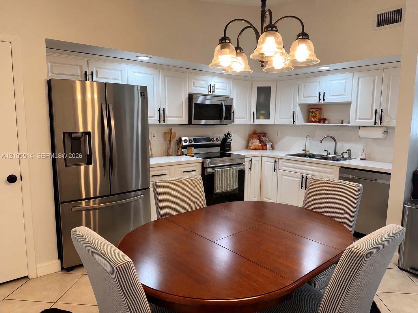Kitchen with white cabinets and stainless appliances, viewed over a round wood dining table and striped chairs.