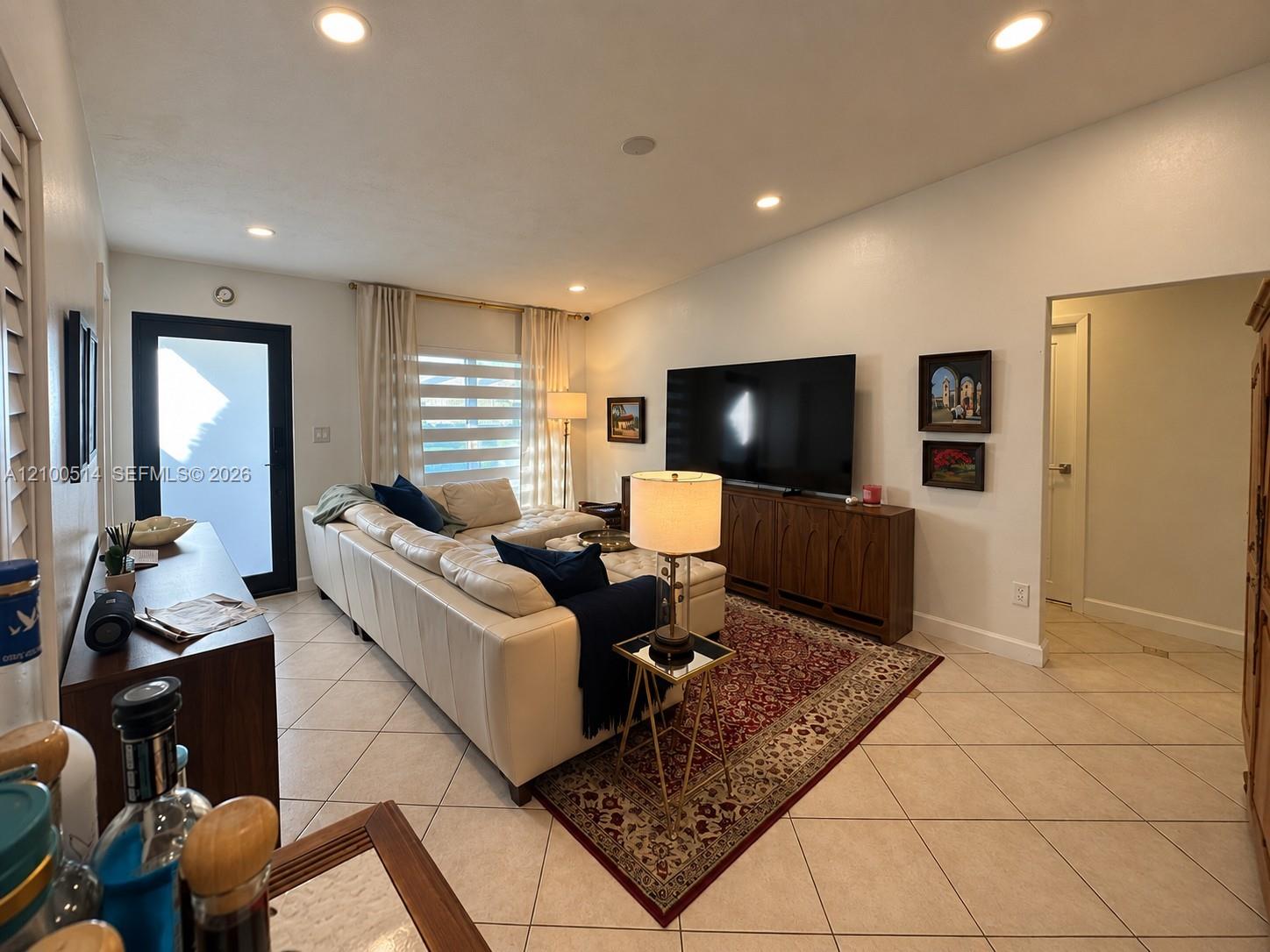 Furnished living room with a cream sectional, large television, and patterned rug.