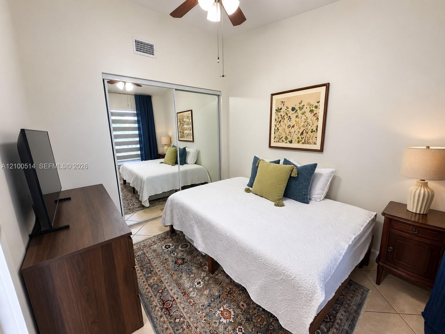Bedroom with a white-covered bed, mirrored closet doors, and patterned rugs.