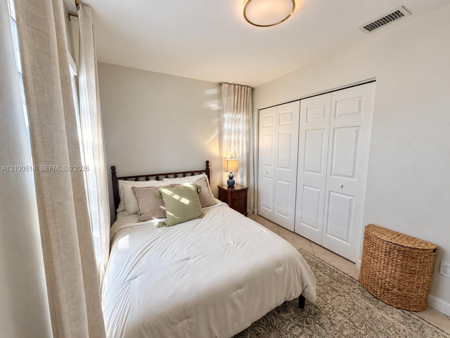 Staged bedroom with a white bed, paneled closet doors, and a patterned rug.