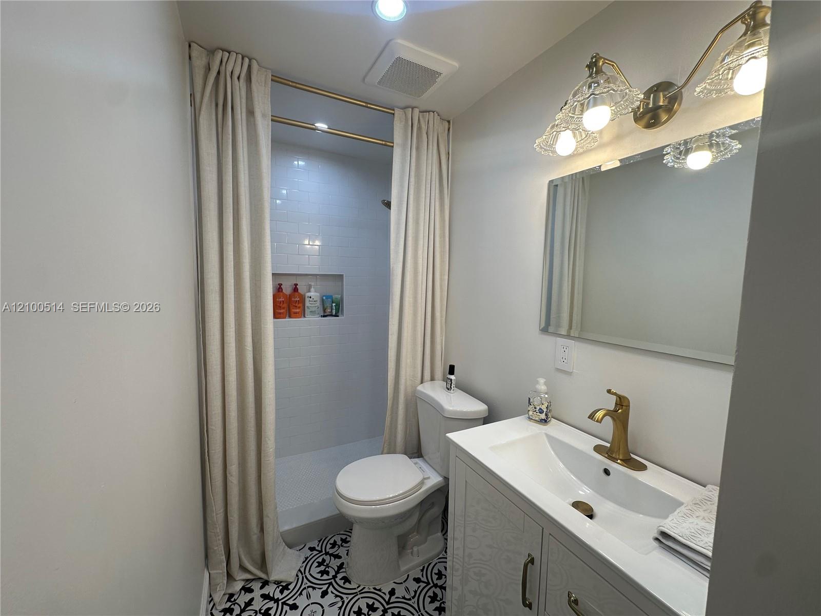 Bathroom with a white vanity, gold fixtures, curtained subway-tile shower, and patterned floor.
