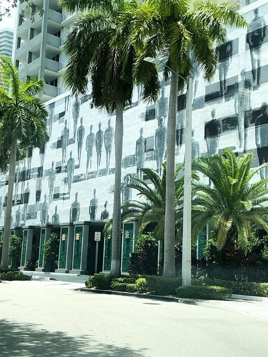Condominium exterior with a mural of human figures, glass entrances, and palm trees.