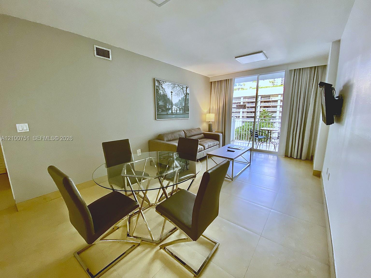 Furnished living and dining area with a glass table and balcony doors.