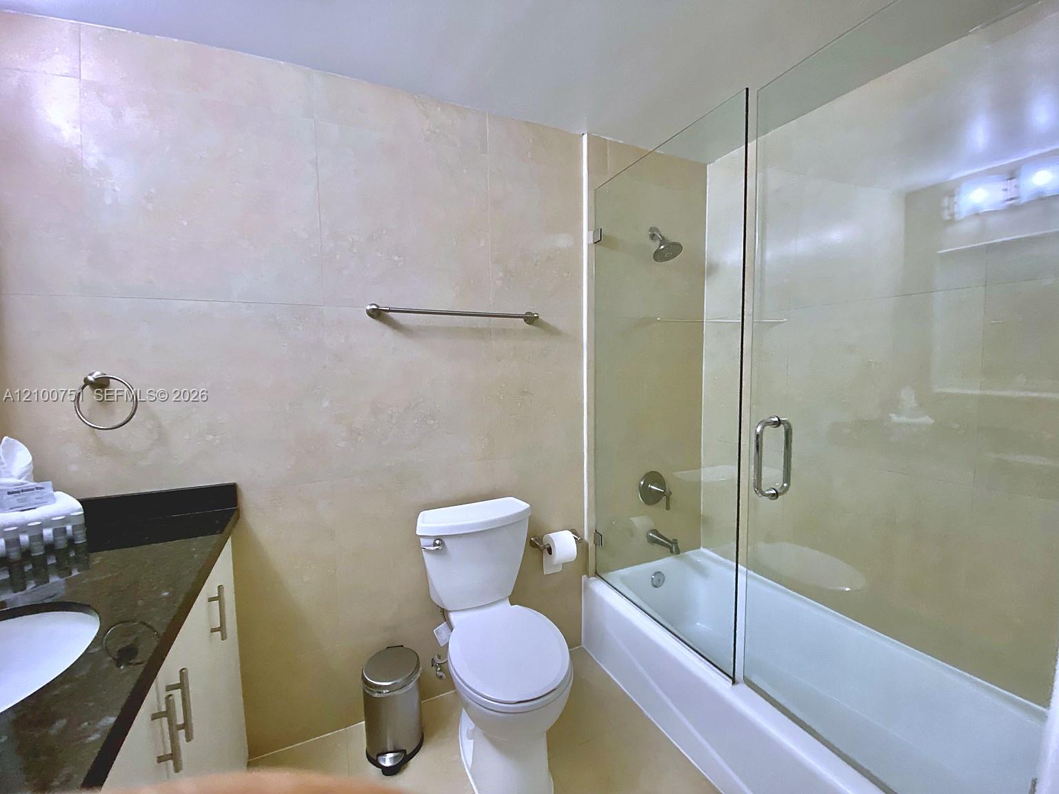 Bathroom with a glass-enclosed tub and shower, toilet, and dark stone vanity.