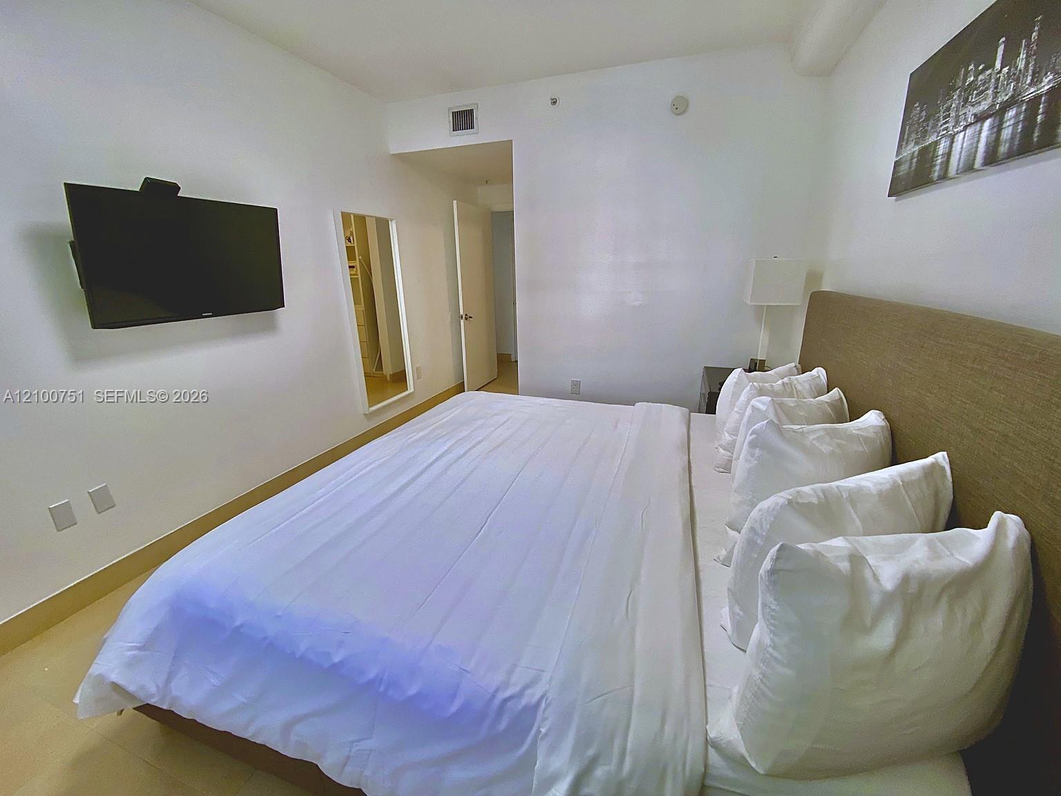 Bedroom with a neatly made bed, upholstered headboard, and wall-mounted television.