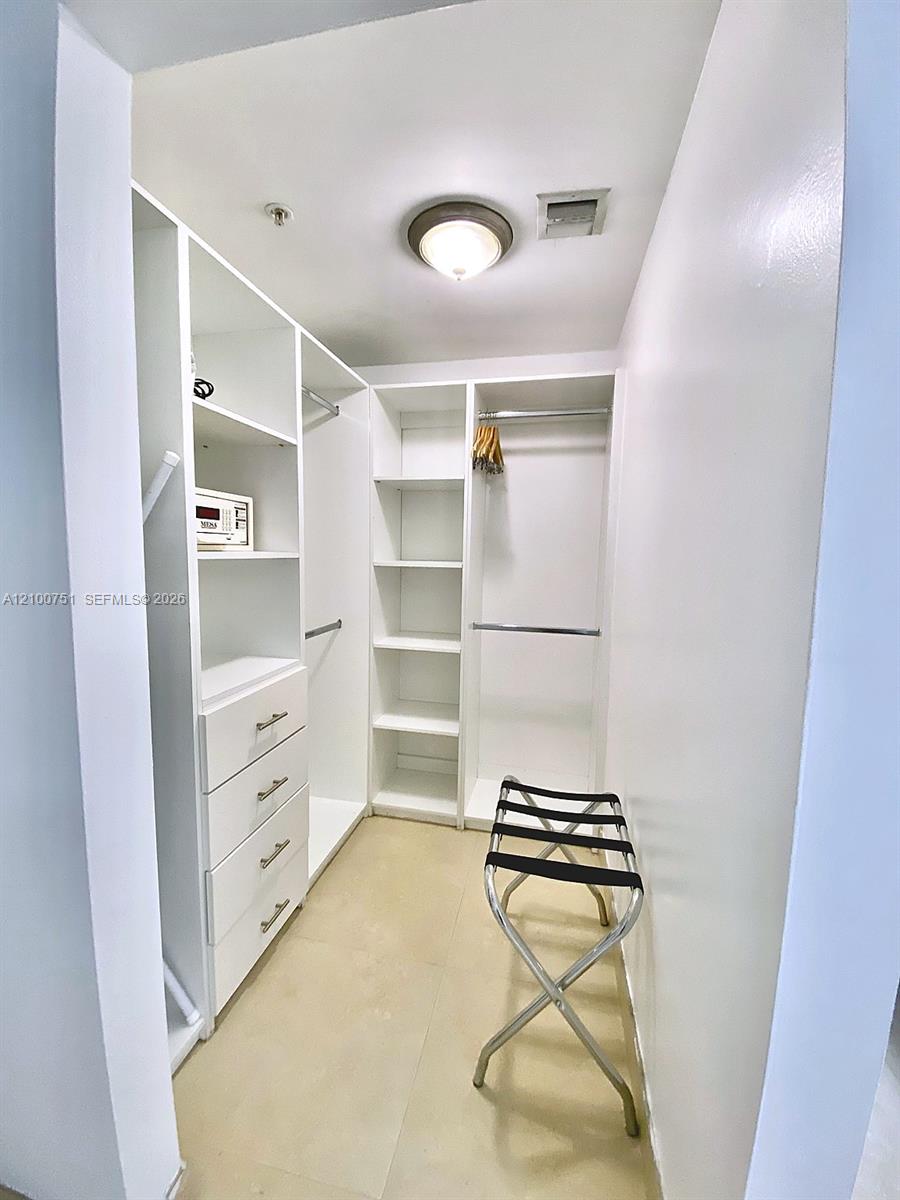 Walk-in closet with built-in shelving, drawers, hanging rods, and a folding luggage rack.