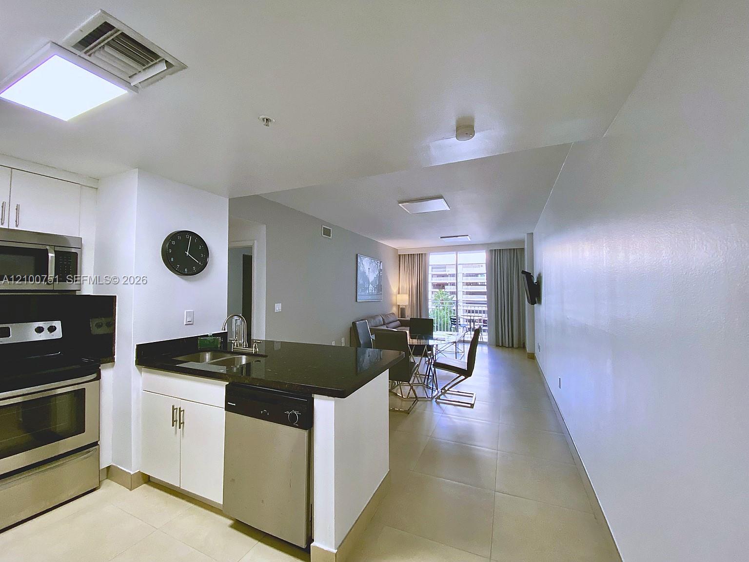 Open kitchen and living area with black granite island, stainless appliances, and balcony doors.