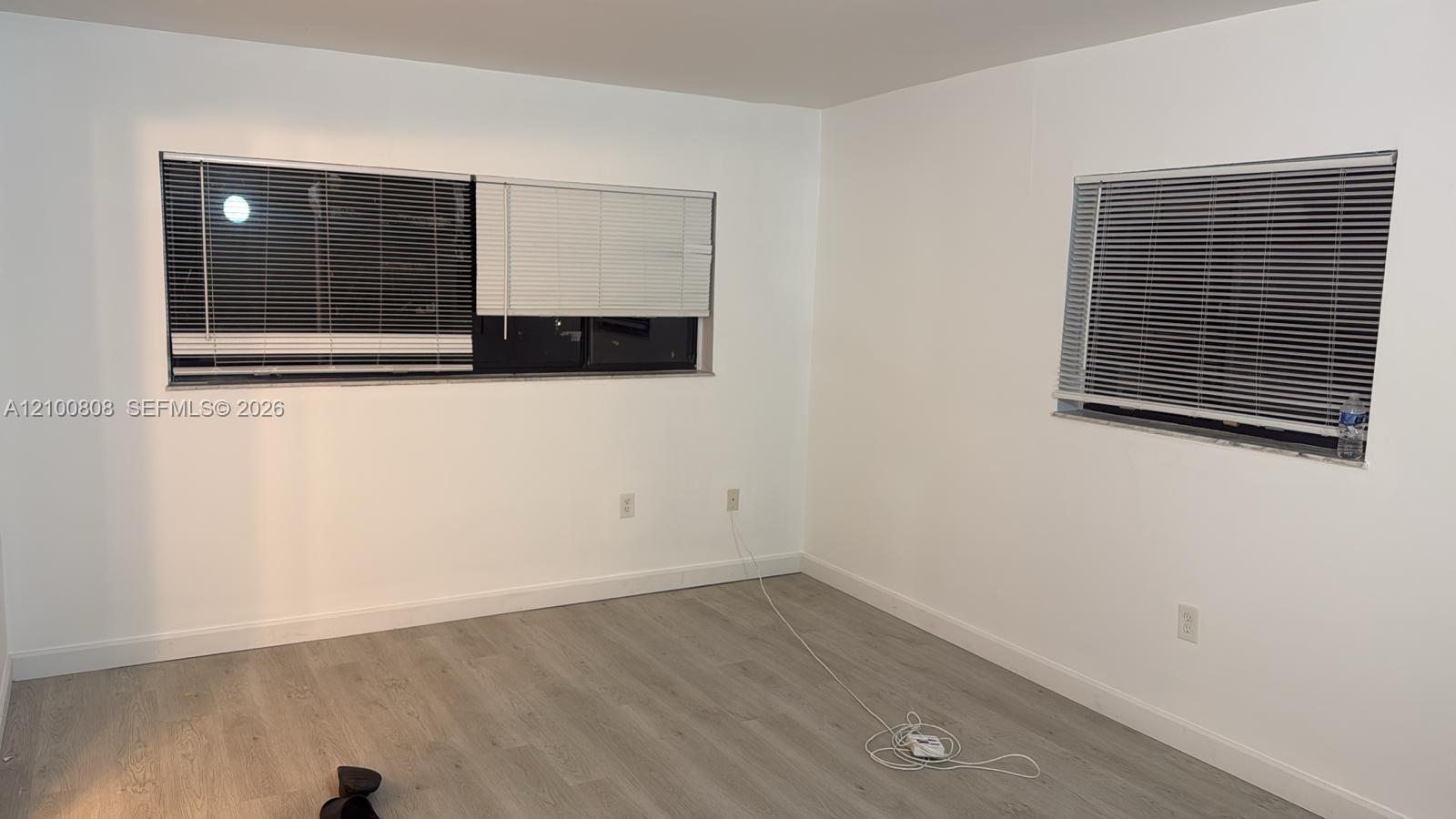 Empty room with gray wood-look flooring and two windows with blinds.