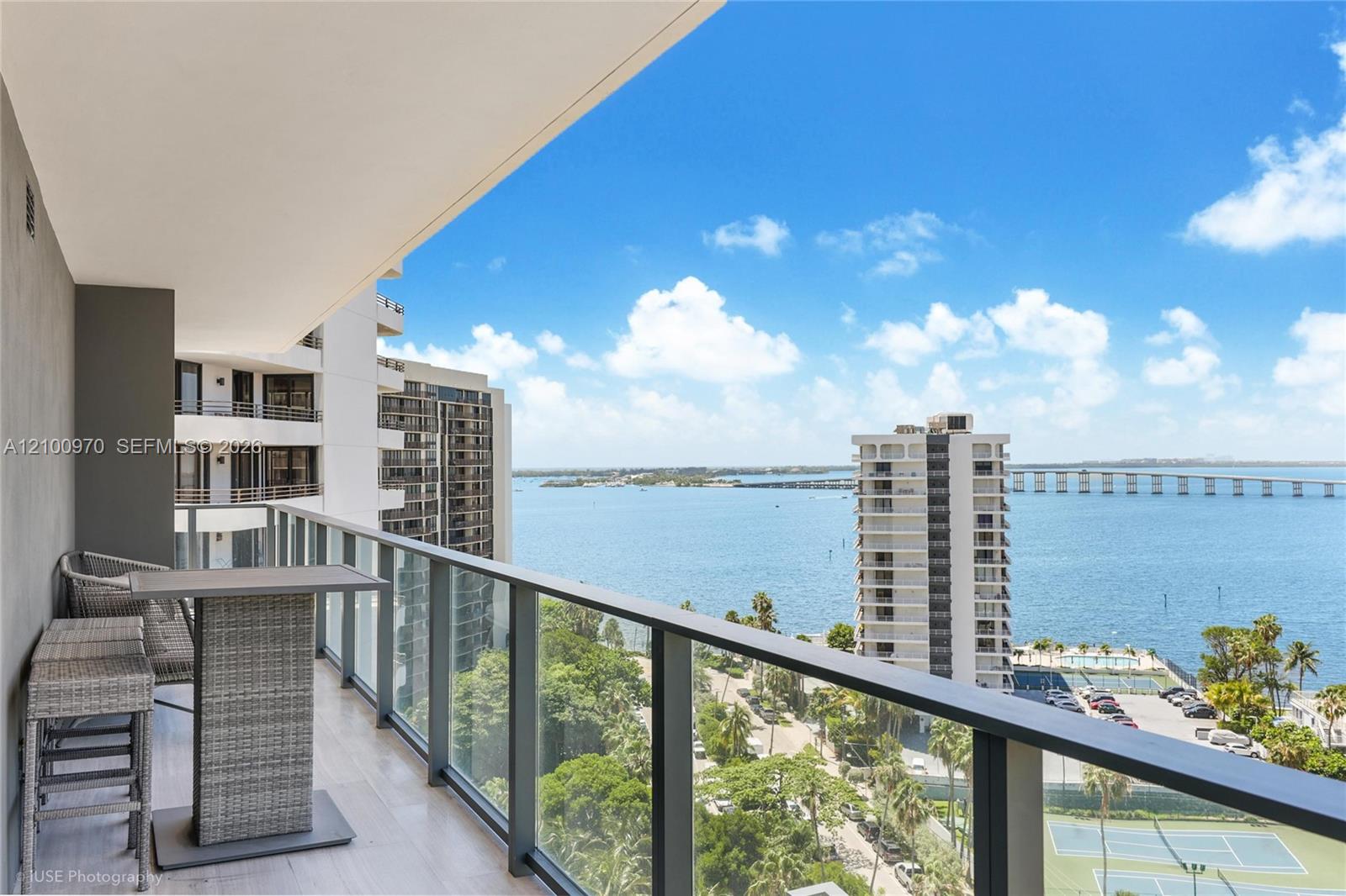 Furnished balcony overlooking Biscayne Bay, with glass railings and neighboring towers.