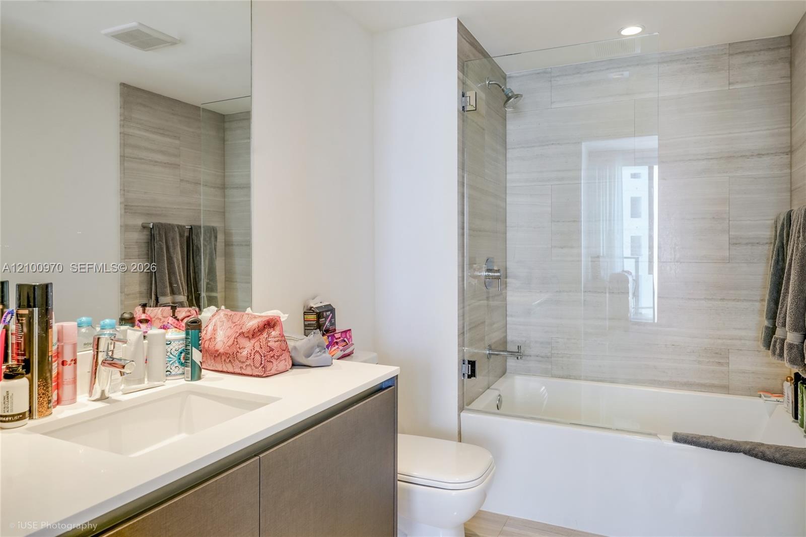 Bathroom with a white vanity and mirror beside a glass-panel tub and light gray tiled surround.