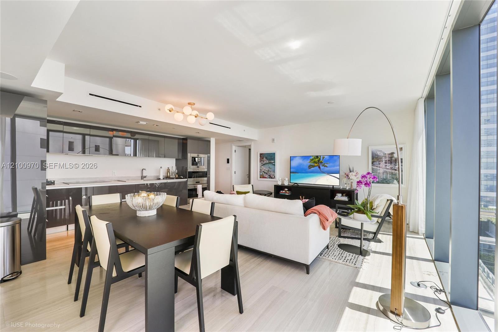 Open-plan condo with a glossy dark kitchen, dining table, white sofa, and floor-to-ceiling windows.