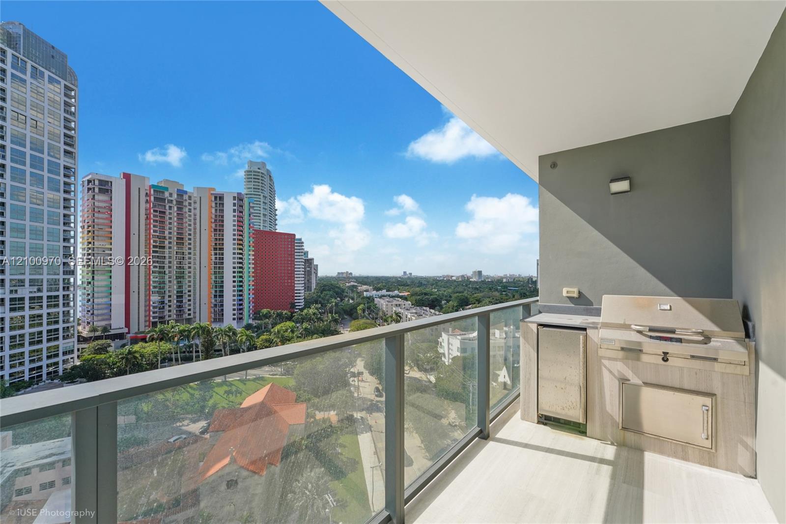 Condo balcony with a built-in grill and views of Miami high-rises and greenery.