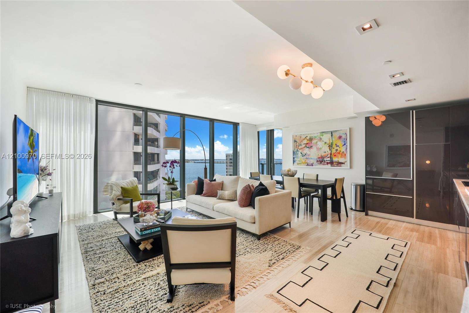 Furnished living and dining room with floor-to-ceiling windows overlooking the water.