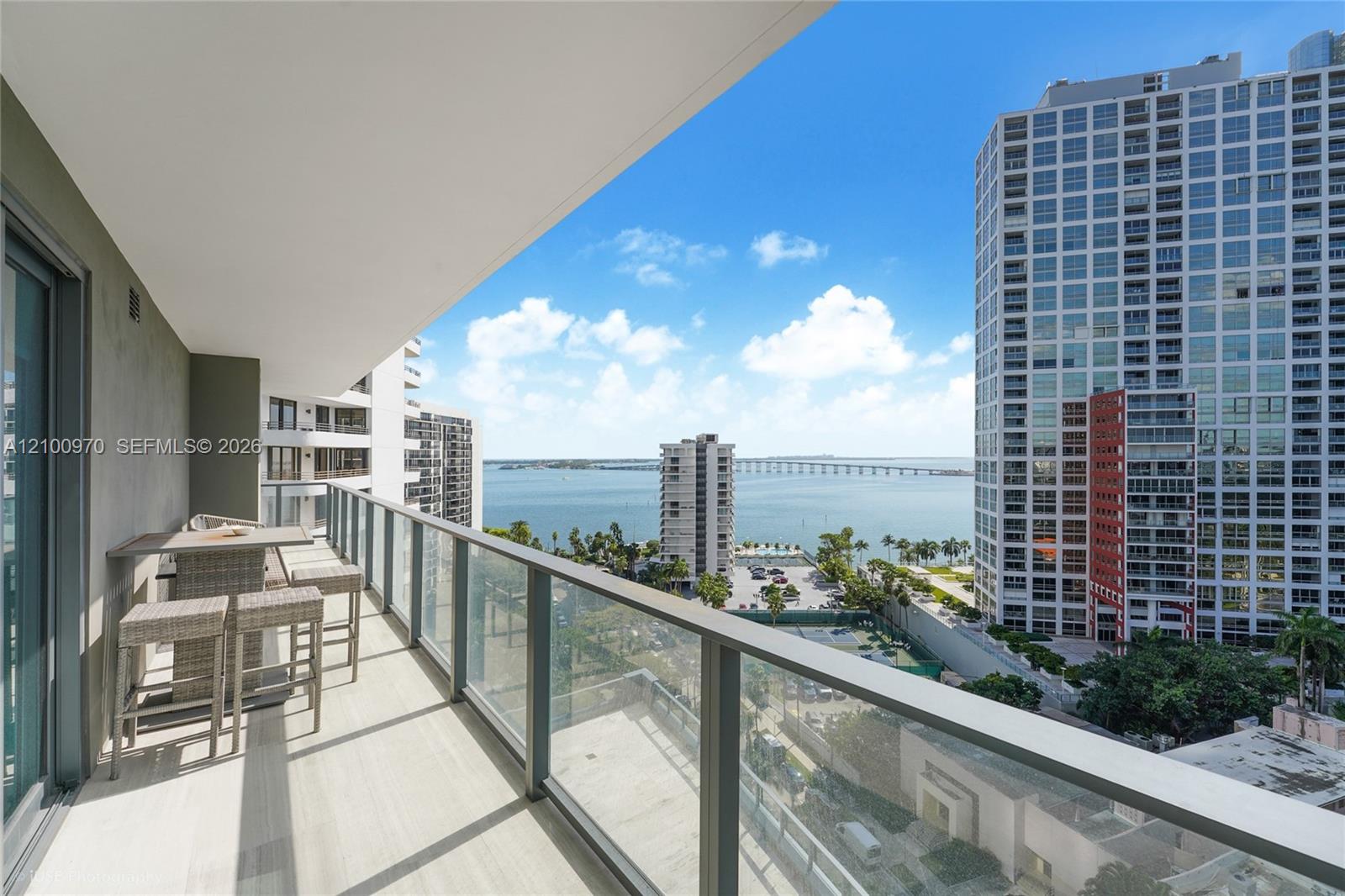 Condo balcony with an outdoor dining set overlooking water, a bridge, and Miami high-rises.