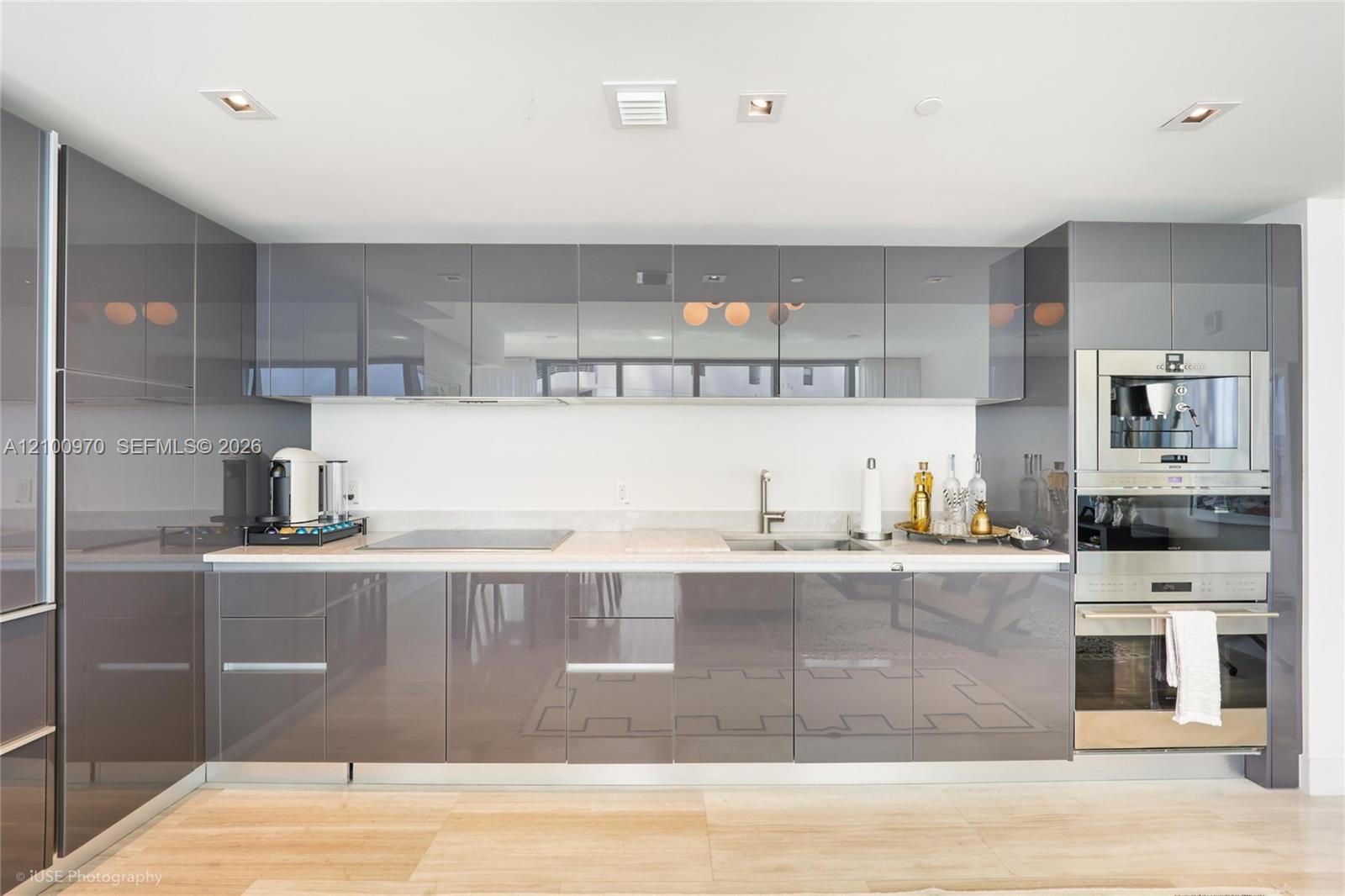 Modern kitchen with glossy gray cabinets, mirrored uppers, and stainless steel built-in appliances.