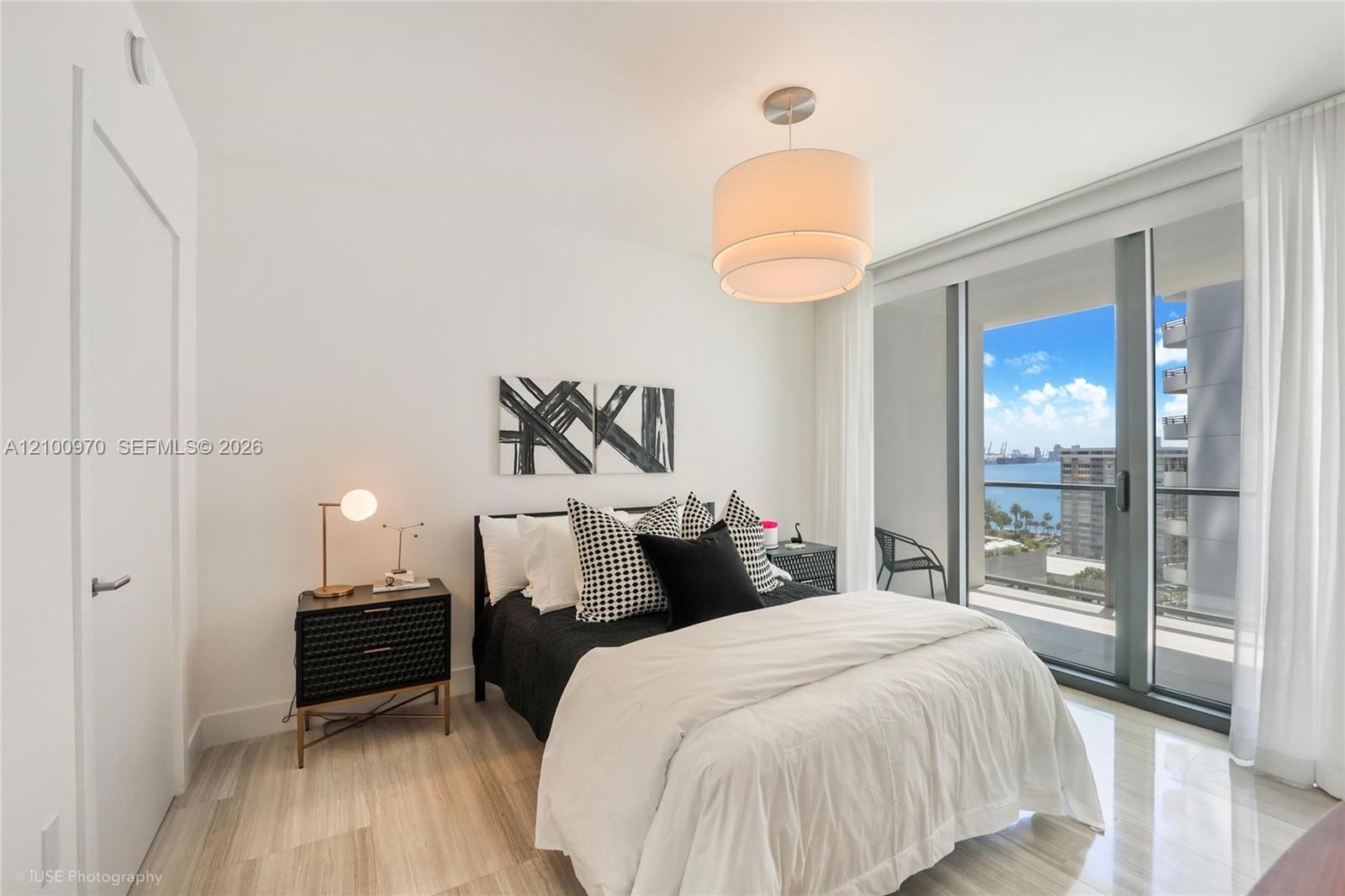 Staged condo bedroom with black-and-white bedding and balcony doors overlooking the water.