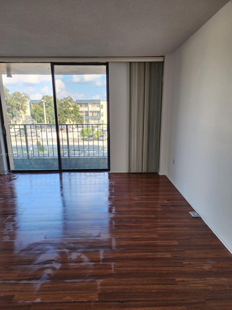 Empty room with glossy dark wood floors and sliding glass doors leading to a balcony.